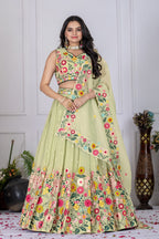 A woman models a light green embroidered Indian ethnic outfit, featuring a sleeveless crop top, a flared skirt with colorful floral patterns, and a matching dupatta, set against a white paneled wall background.